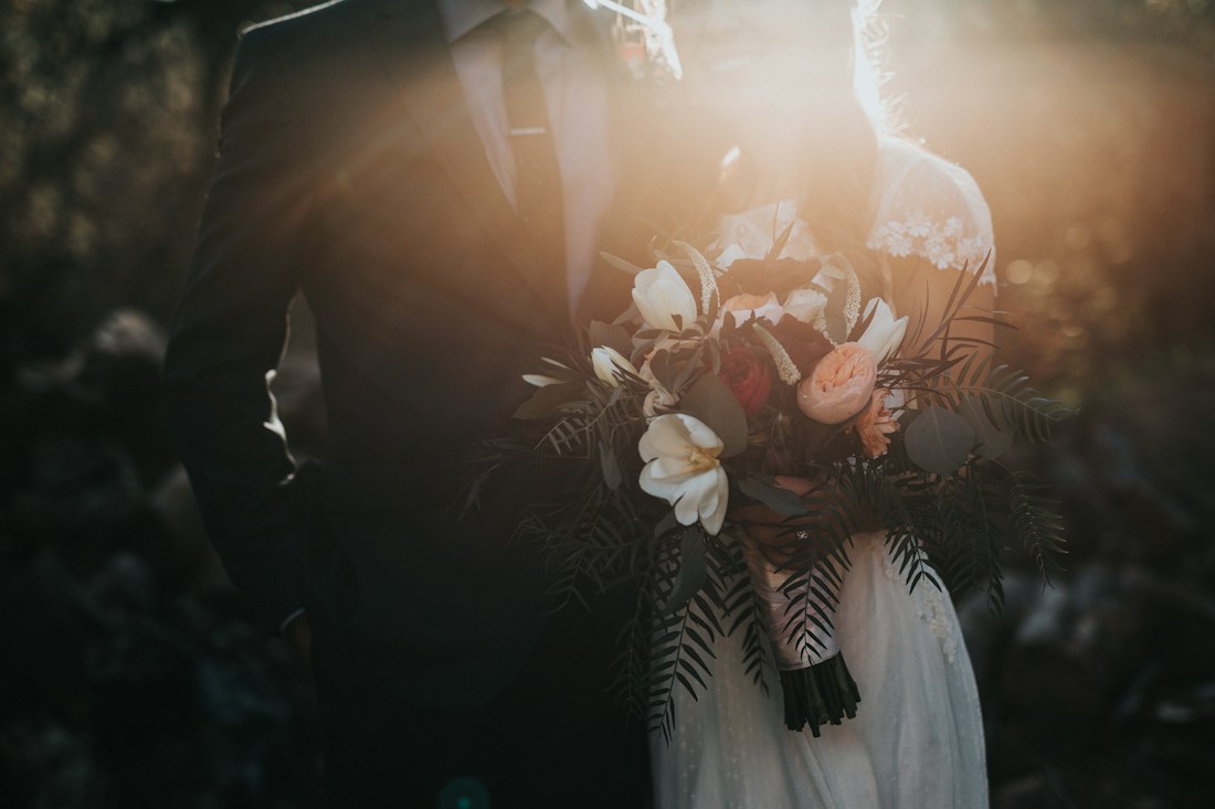 A newly married couple holding a bouquet in the warm afternoon light